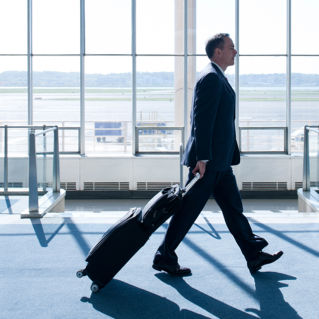 Business man with rolling suitcase walking in airport terminal.
